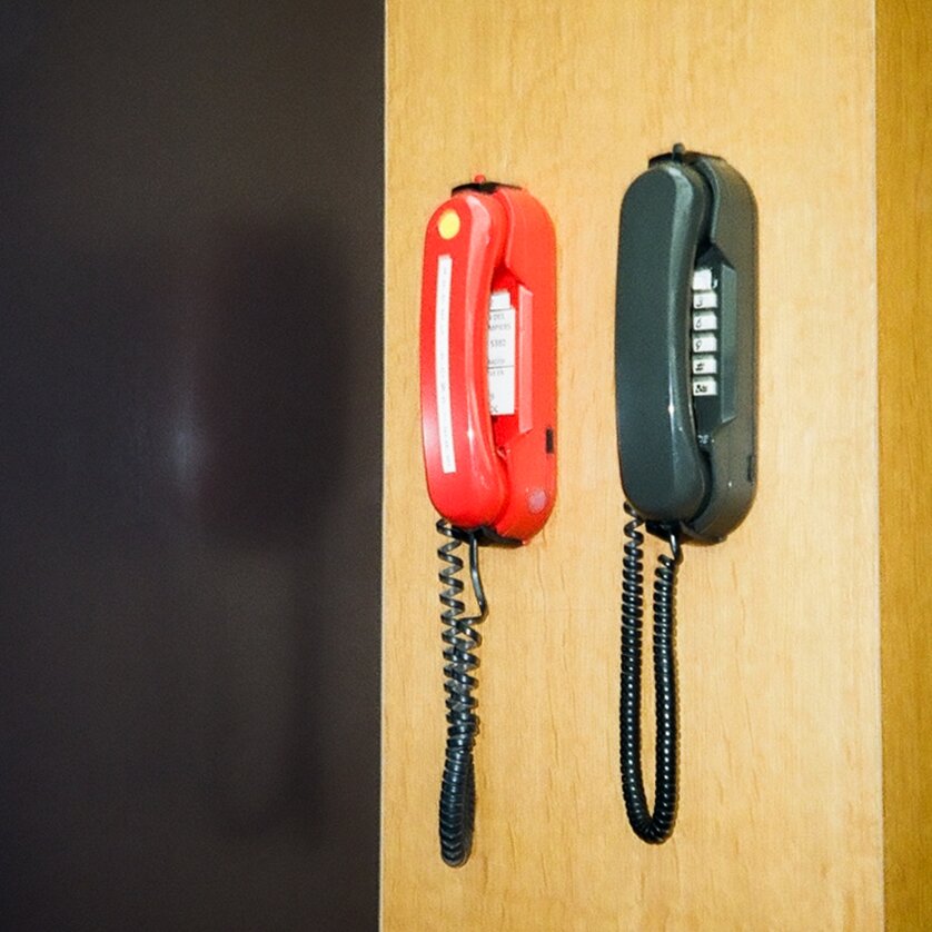 Zwei Telefonhörer, einer rot und einer schwarz, hängen an einer Wand.