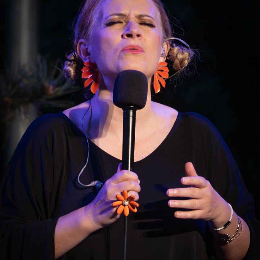 Eine Sängerin singt leidenschaftlich ins Mikrofon mit Blumenohrringen. | © Michael Sticher