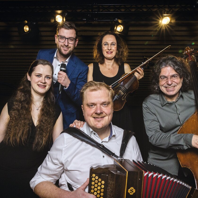 Fünf Musiker posieren mit Harfe, Geige, Akkordeon und Kontrabass. | © funTASTIG