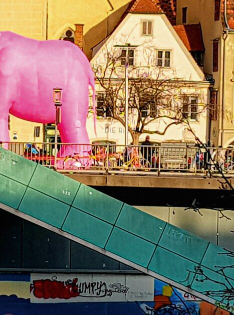 Ein großes rosa Tier steht auf einer Brücke in Graz, umgeben von Gebäuden. | © Ines Pamperl  Scroll durch dein Leben!