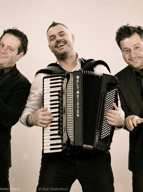 Drei Musiker posieren gemeinsam mit Trompete und Akkordeon. | © личен архив - Boki Radenkovic - IA gen