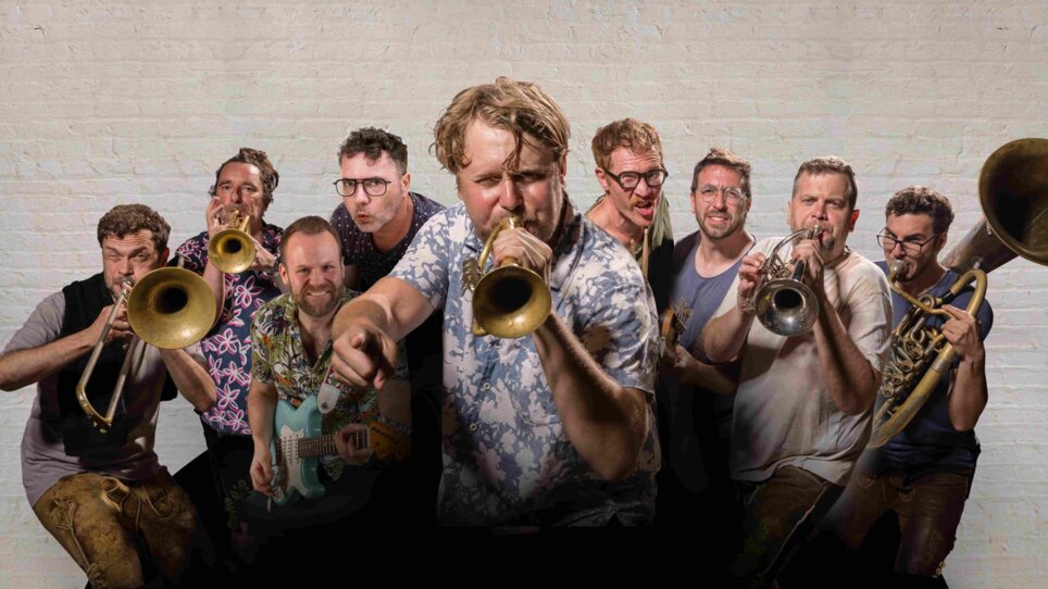 Eine Gruppe von Musikern mit Trompeten und einer Gitarre posiert energetisch für das Foto. | © David Königsmann