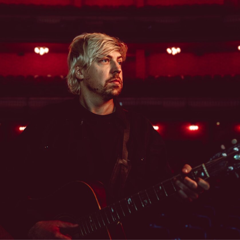 Ein Musiker steht mit Gitarre in einem leeren Theater. | © Sophie Seybold