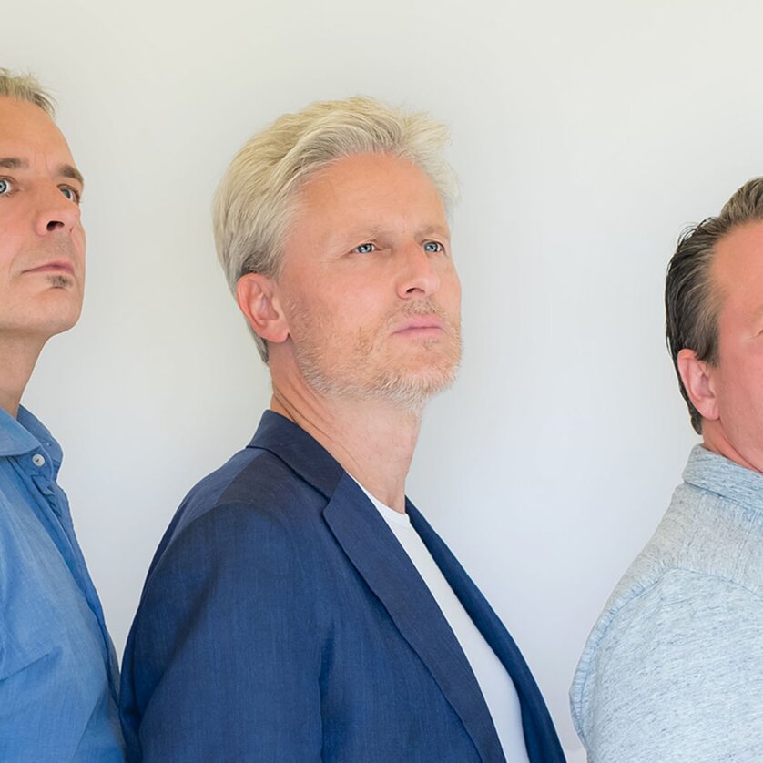 Drei Männer stehen nebeneinander, mit ernstem Blick in verschiedene Richtungen. | © Whirlphoto