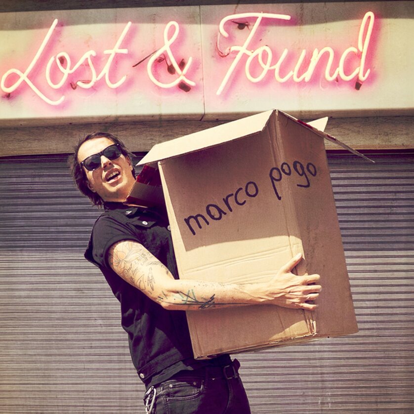 Junger Mann hält einen großen Karton mit der Aufschrift 'marco pogo' vor einem Lost & Found-Schild. | © Marco Pogo