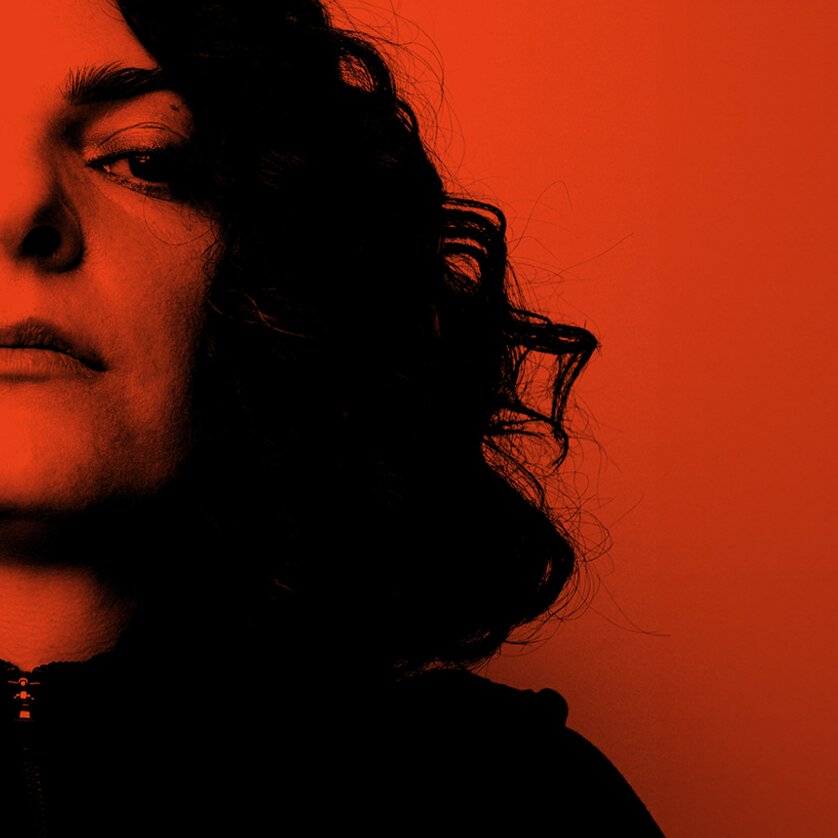 Eine Frau mit lockigem Haar sieht ernst in die Kamera, Hintergrund rot. | © Murat Aslan