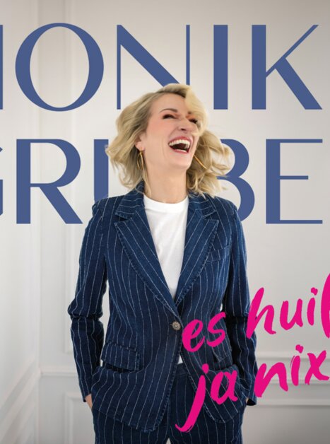 Monika Gruber lacht in einem blauen Streifenanzug. | © Starupphoto