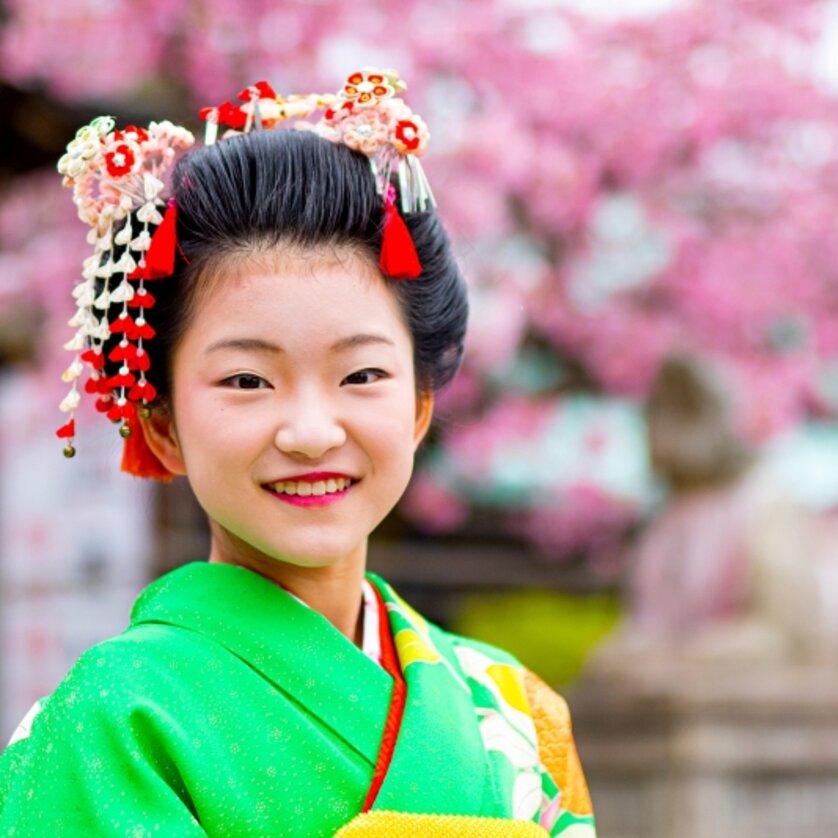 Ein lächelndes Mädchen in einem bunten Kimono vor kirschblühenden Bäumen. | © Bastian Maria
