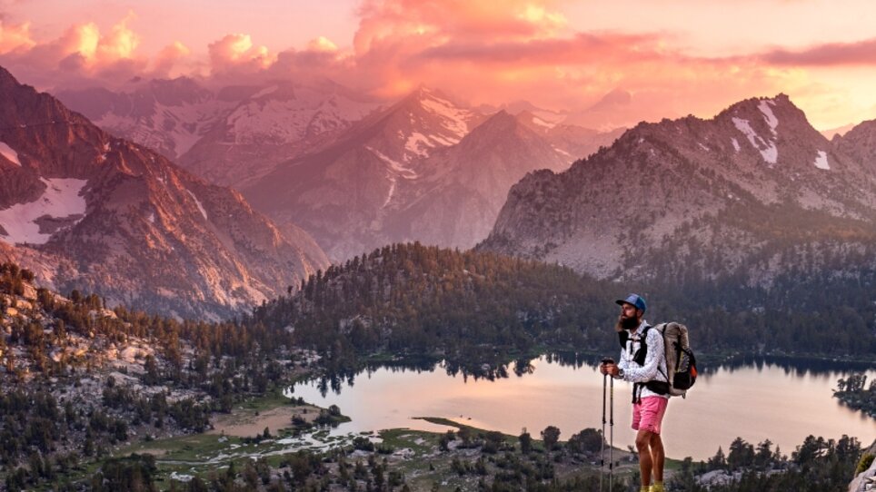 Ein Wanderer steht bei Sonnenuntergang über einem Bergsee und bewundert die Aussicht. | © Florian Astor