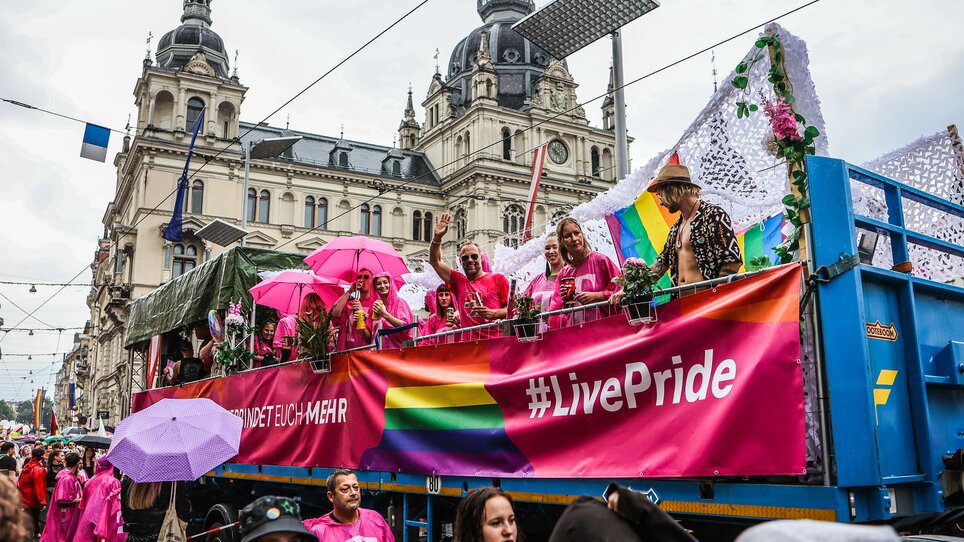 Participants of CSD Graz with rainbow flags and pink umbrellas on a float. | © Sebastian Neugebauer