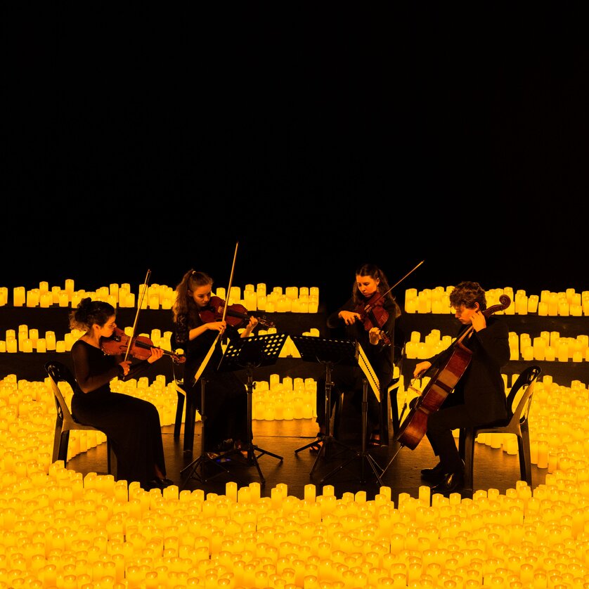 Four musicians performing on a stage surrounded by candles. | © Fever
