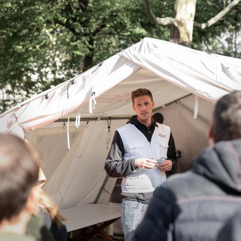 Ein Mitarbeiter von "Ärzte ohne Grenzen" erklärt etwas vor einem Zelt bei einer Informationsveranstaltung. | © Ärzte ohne Grenzen - Ramon Ritter