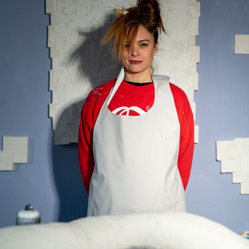 Künstlerin Andrea Kurtz mit rotem Pullover und weißer Schürze - steht vor einem ihrer Kunstwerke. | © Fabsabmedia - die Blumenfotografin