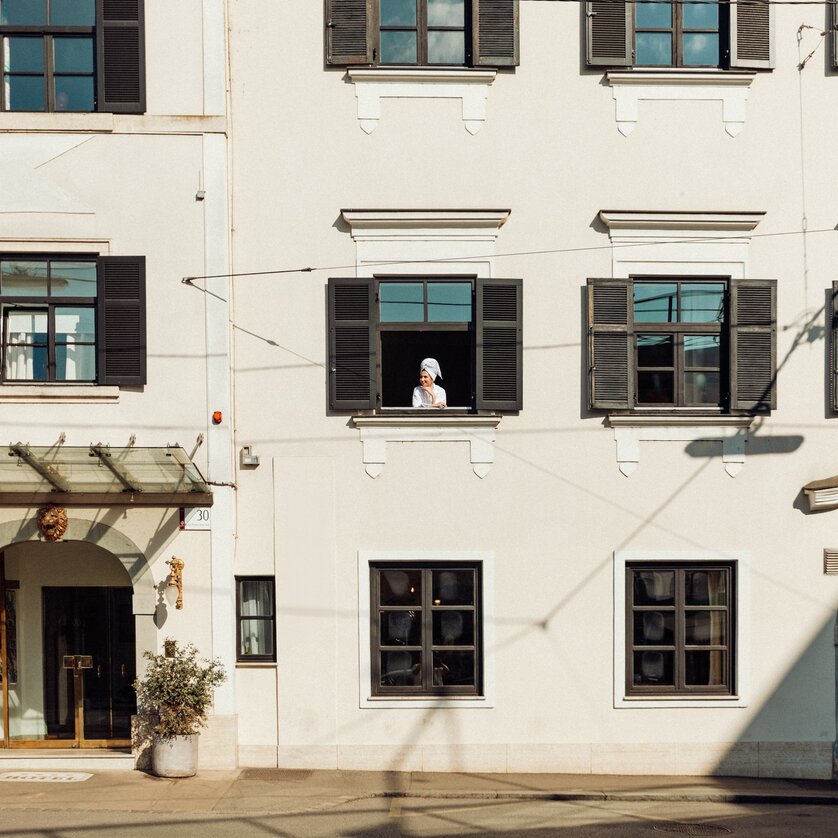Eine Person im Bademantel lehnt an einem Fenster des Schlossberghotels in Graz und sieht aus dem Fenster. | © Schlossberghotel Graz - KYRI