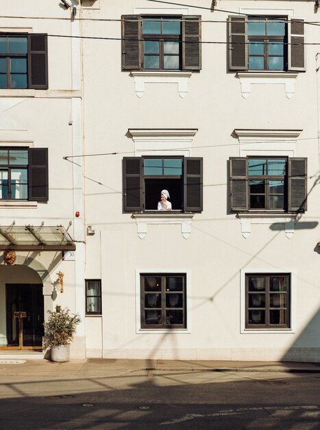 Eine Person im Bademantel lehnt an einem Fenster des Schlossberghotels in Graz und sieht aus dem Fenster. | © Schlossberghotel Graz - KYRI