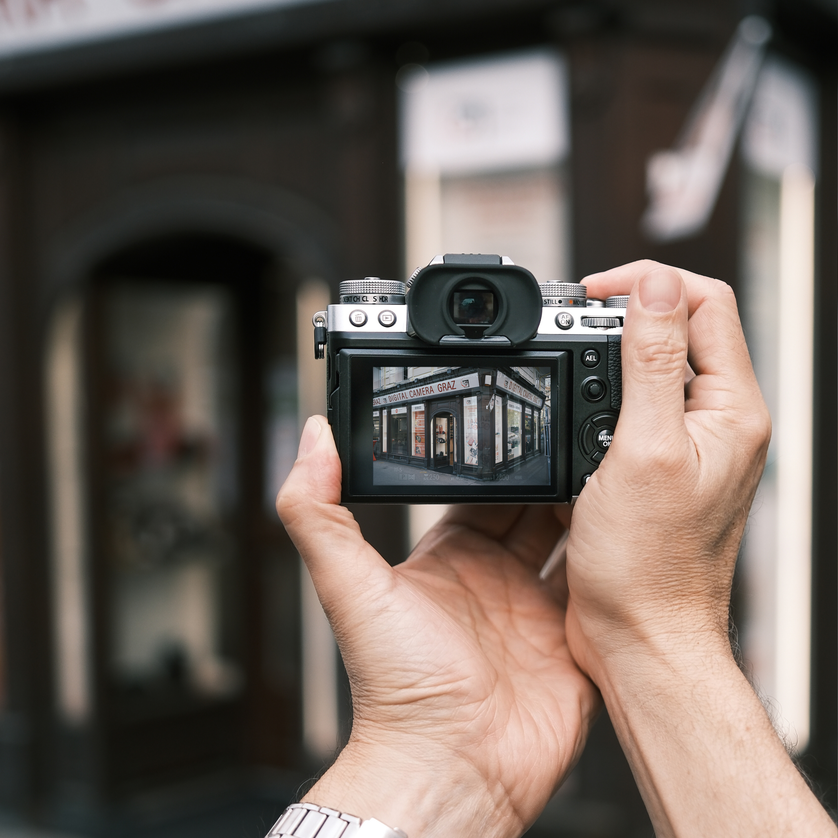 Eine Person fotografiert einen Blick auf ein Ladenschild mit einer Kamera. | © Maria Alberer