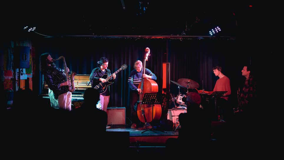 A jazz band plays on a dimly lit stage in front of an audience. | © Kuro Simon