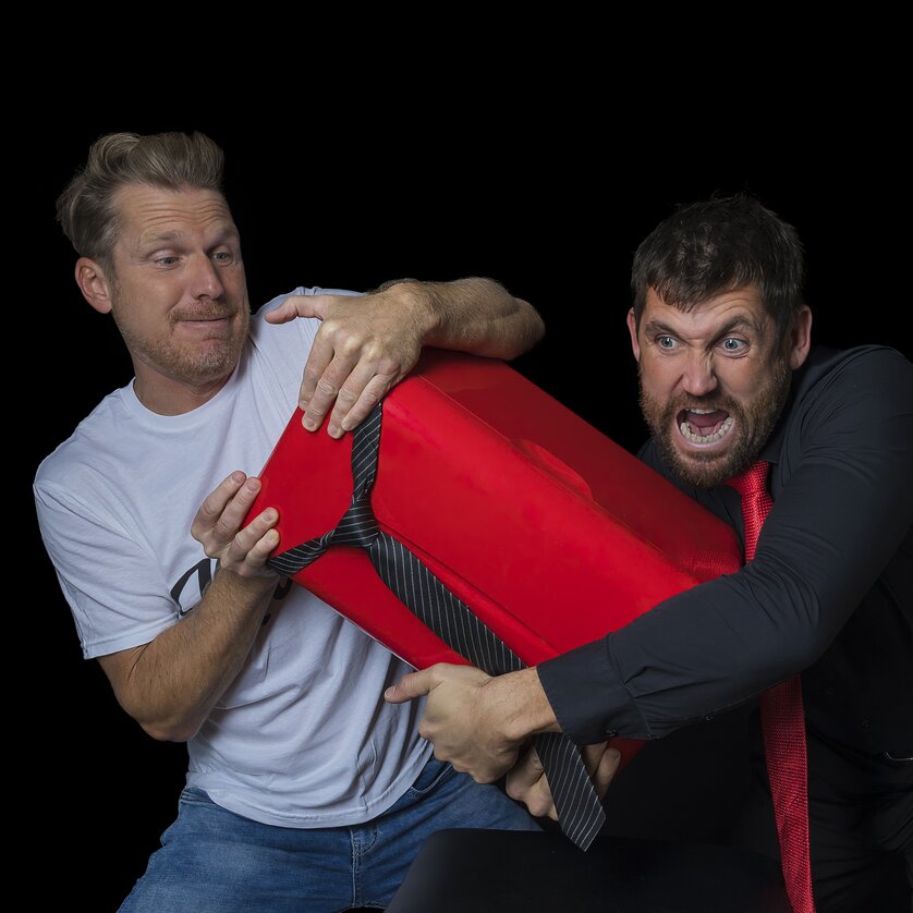 Zwei Männer kämpfen um ein großes rotes Geschenk. | © Richard Weiß Photography