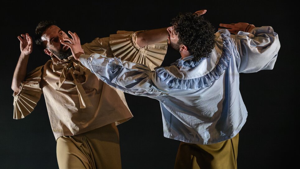 Two dancers in elegant attire engage in a powerful interaction on stage. | © Int. Bühnenwerkstatt