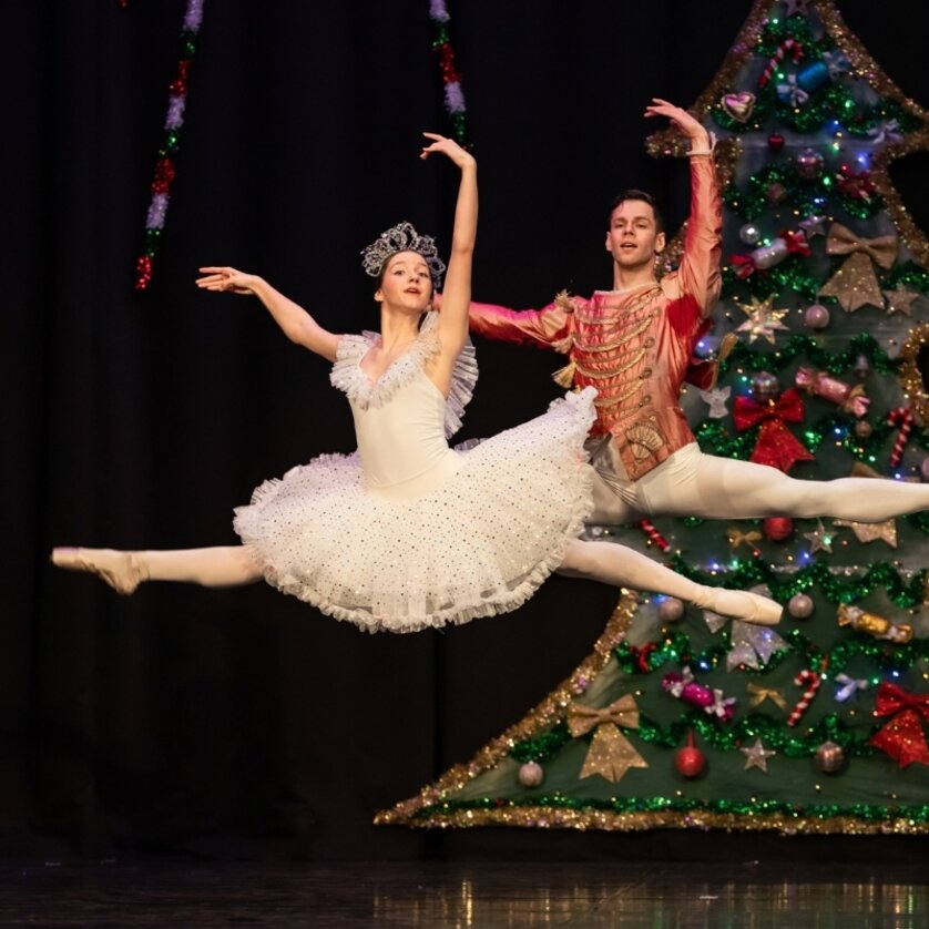 Two ballet dancers in a jump position in front of a decorated Christmas tree. | © Austrian Youth Ballet