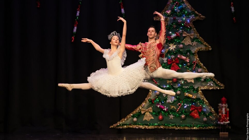 Two ballet dancers in a jump position in front of a decorated Christmas tree. | © Austrian Youth Ballet