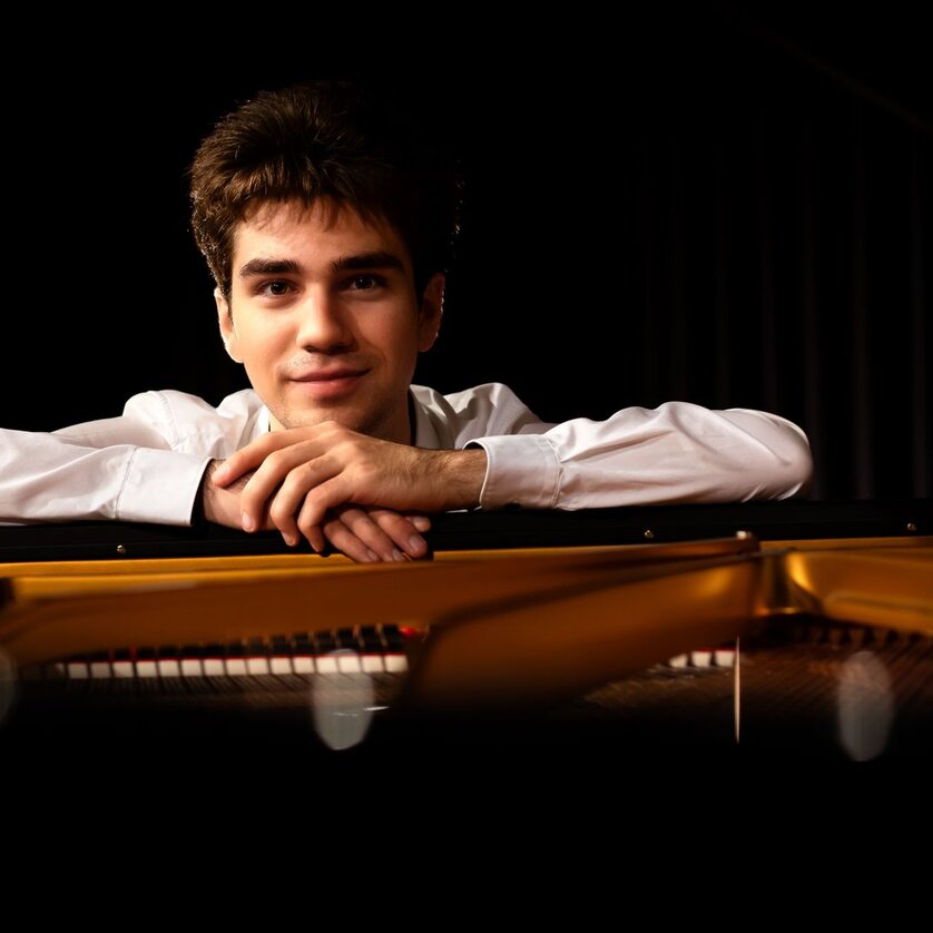 A young man leans on a piano and smiles. | © Christoph Preiss