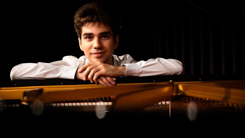 A young man leans on a piano and smiles. | © Christoph Preiss