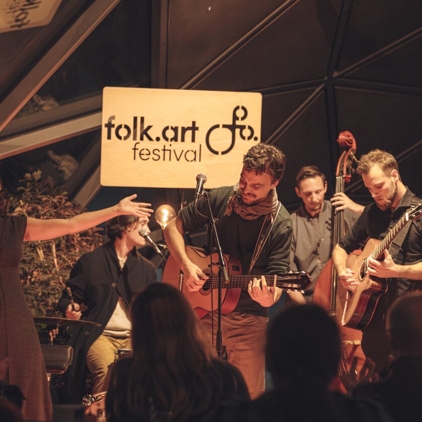 Fünf Musiker mit Gitarren, Kontrabass und Schlagzeug spielen auf einer Bühne | © Madelaine-Marie