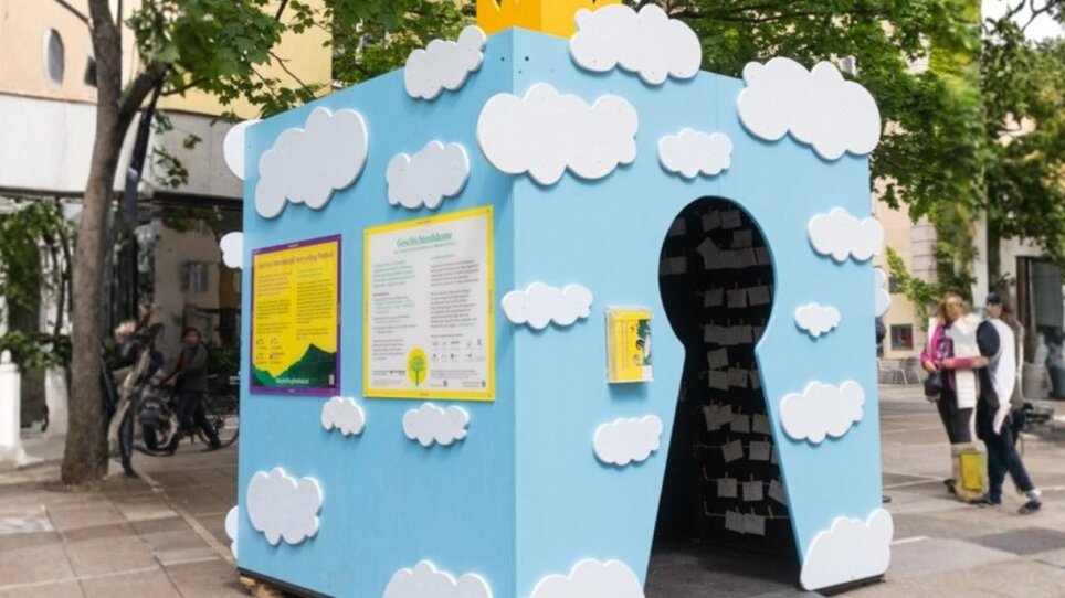 A light blue hut decorated with white cloud motifs and a yellow crown, designed to represent a fairytale castle as part of the ‘Graz erzählt’ festival. | © Moritz Pirker