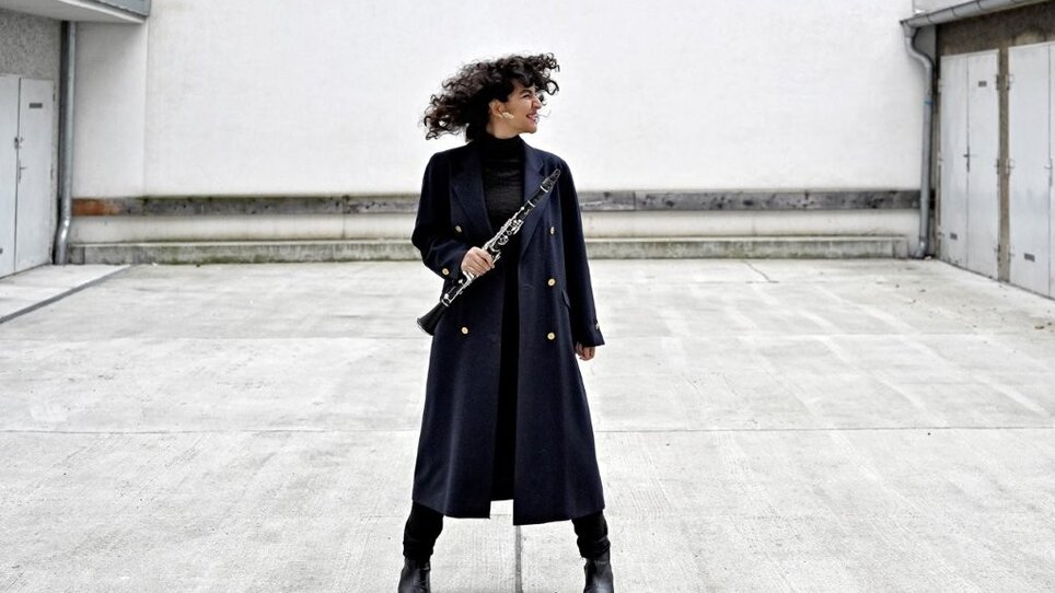 Mona Matbou Riahi is holding a clarinet in an urban setting. | © Nina Streets
