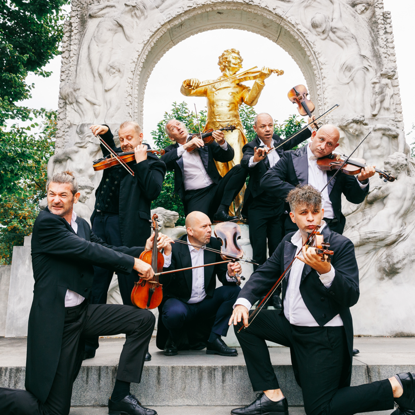 Eine Gruppe von Musikern posiert mit Geigen vor einer Statue. | © Maria Frodl