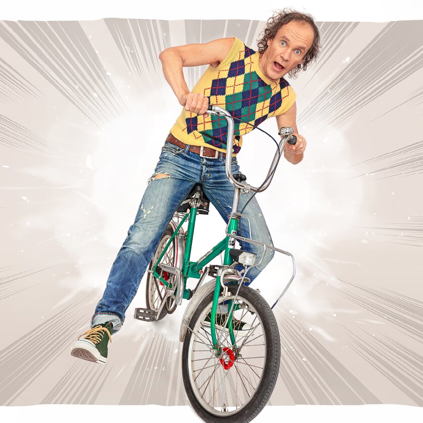 Ein Mann in buntem Outfit fährt begeistert auf einem Fahrrad. | © Olaf Schubert Pressestelle