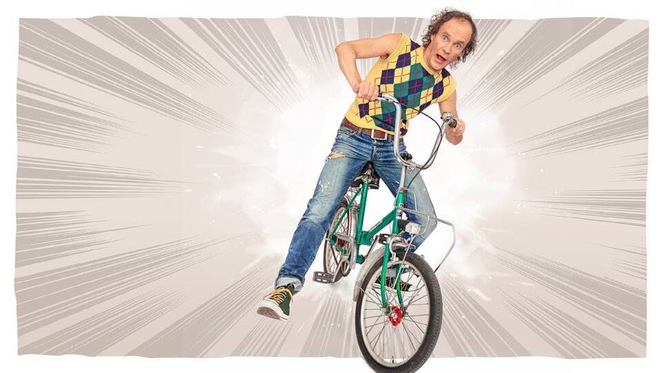 Ein Mann in buntem Outfit fährt begeistert auf einem Fahrrad. | © Olaf Schubert Pressestelle