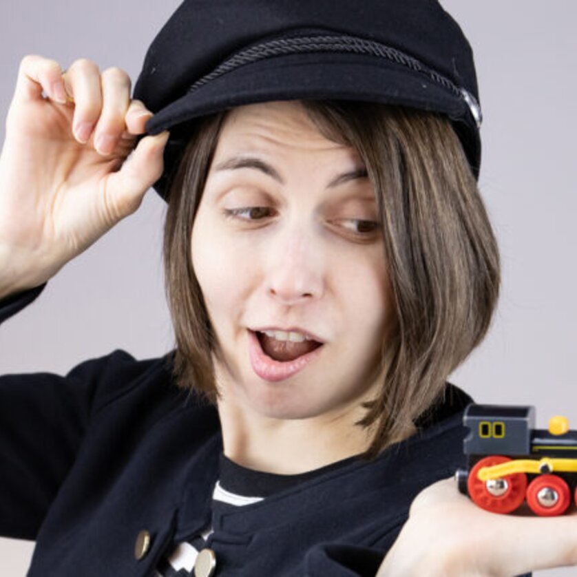 Eine Person in Uniform zeigt erstaunt auf eine kleine Spielzeuglok. | © Magda Leeb