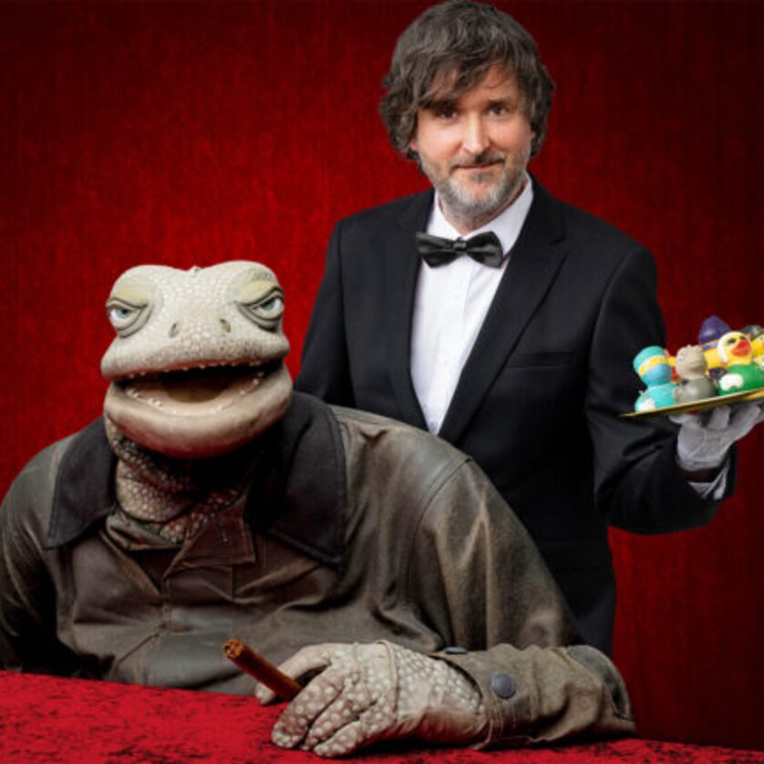 Ein Frosch im Anzug sitzt an einem Tisch, während ein Kellner einen Teller serviert. | © Paul Jackel