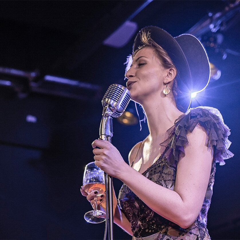 A woman singing with a microphone in hand and holding a wine glass. | © Lucija Novak