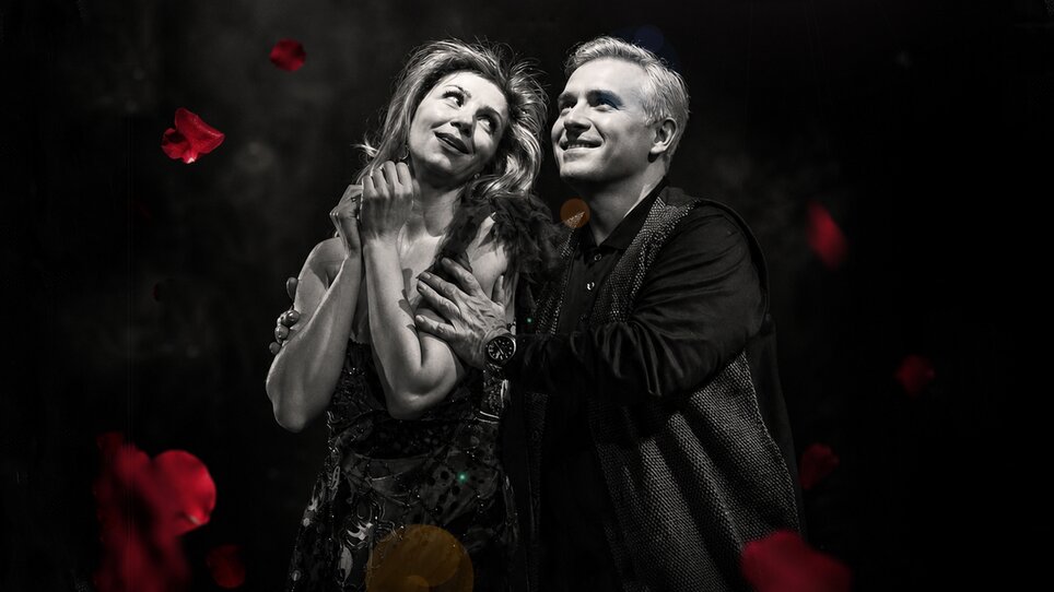 A couple showcases an emotional scene against a dark background with rose petals. | © Lucija Novak