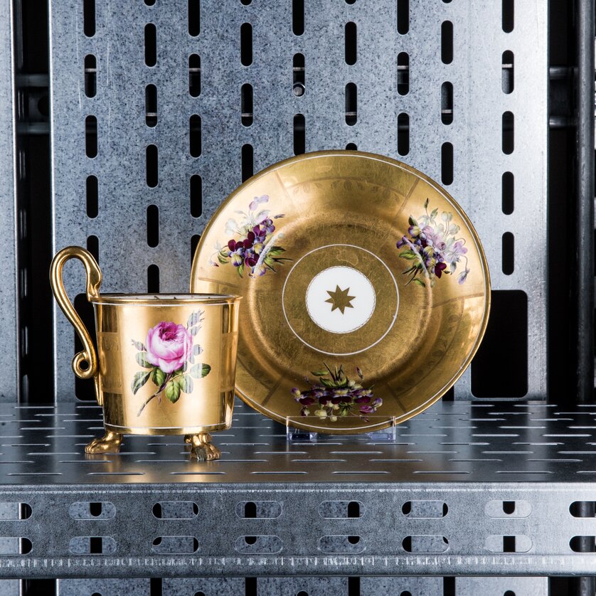 Genussreise im Museum für Geschichte I Tischlein deck dich | © Markus Mansi_MOMA Ein goldener Becher und Untertasse mit Blumenmotiven auf einem Regal. | © Markus Mansi_MOMA