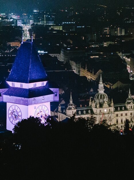 Beleuchtete Stadt Graz bei Nacht mit dem Grazer Uhrturm im Vordergrund. | © Sebastian Reiser
