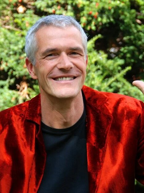 A man in a red jacket smiles and makes hand gestures. | © Beate Hofstadler