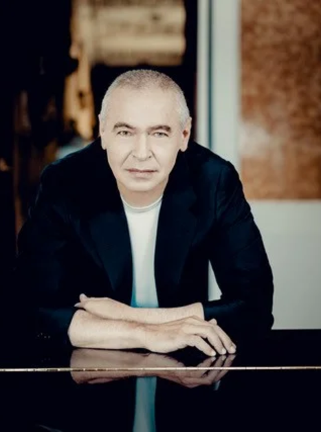 Ein Mann in einem schwarzen Blazer lehnt an einem Klavier. | © Andrej Grilc