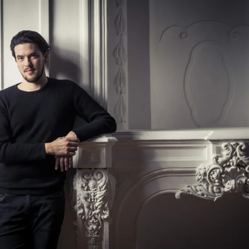Andre Schuen | © Guido Werner Junger Mann in schwarzem Pullover steht neben einer dekorativen Wand. | © Guido Werner