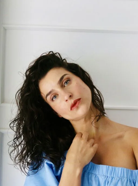 Porträt einer Frau mit lockigem Haar, die eine blaue Bluse trägt. | © Olivia Kahler