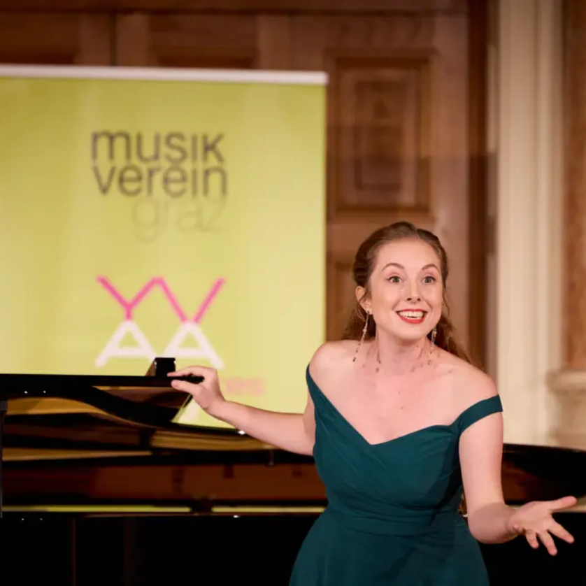 Eine Sängerin mit einem grünen Kleid steht vor einem Klavier und lächelt. | © Kurt Remling
