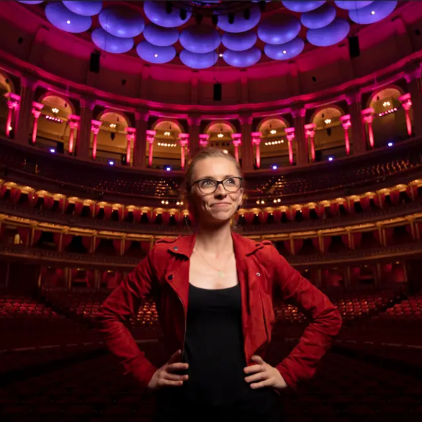 Eine Frau steht im beleuchteten Konzertsaal mit rotem Licht. | © Nick Rutter