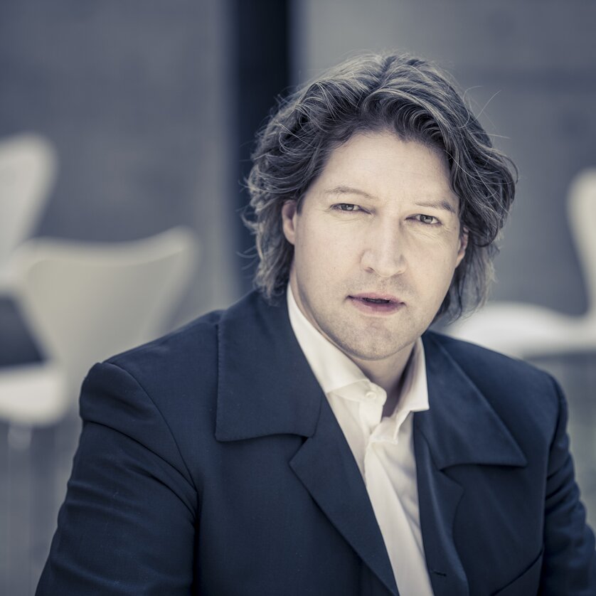 Mann mit lockigem Haar trägt ein weißes Hemd und ein dunkles Sako  | © Christan Jungwirth