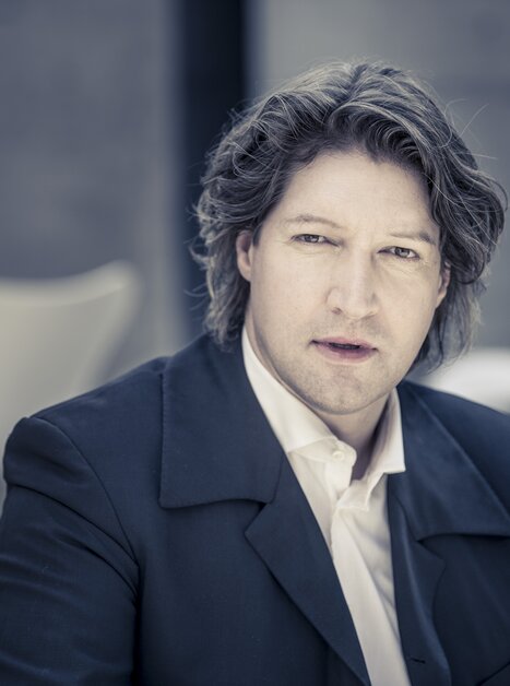 Mann mit lockigem Haar trägt ein weißes Hemd und ein dunkles Sako  | © Christan Jungwirth