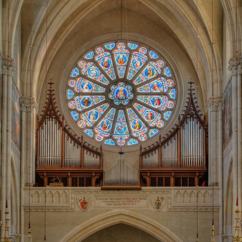Blick auf einen Kirchenraum mit einem bunten Rosettenfenster und einer Orgel. | © Guenther-Deutsch