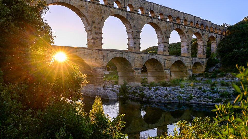 Das historische Aquädukt Pont du Gard reflektiert im Wasser während des Sonnenuntergangs. | © Gerhard Huber