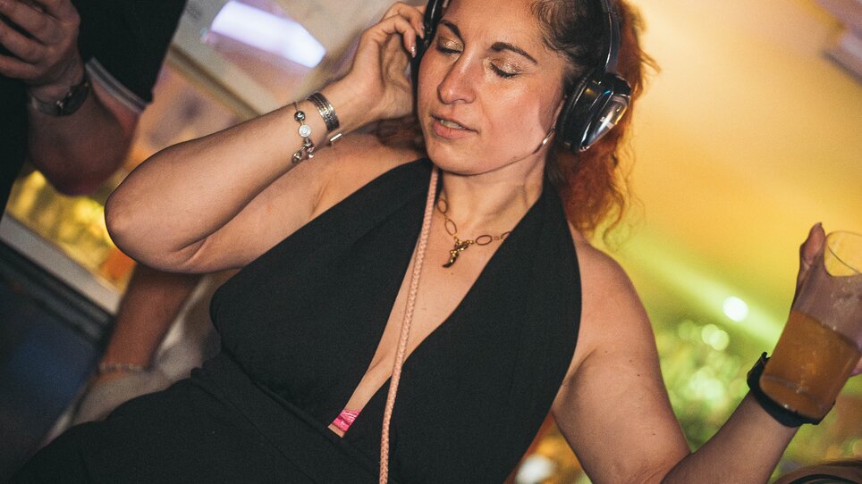 Eine Frau in einem schwarzen Outfit mit Kopfhörern tanzt und hält ein Getränk in der Hand. | © SilentDiscoAustria_Anuar Nakyssov